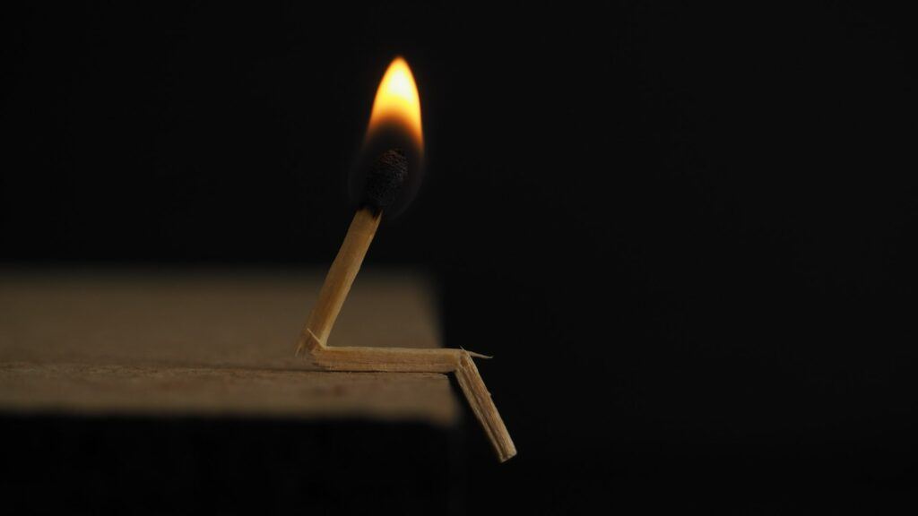 A match broken into a sitting position with its sulfer head burning. Kind of looks like a piano player that has warmed up before starting to play.